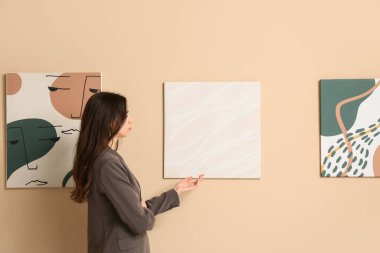Sanat galerisindeki bej duvardaki resimlere bakan genç bir kadın.