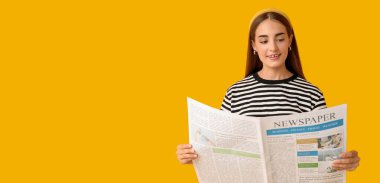 Sarı arka planda gazete okuyan genç bir kadın.