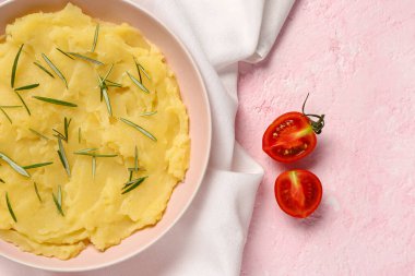 Bir kase lezzetli patates püresi, biberiye ve pembe arka planda domates.