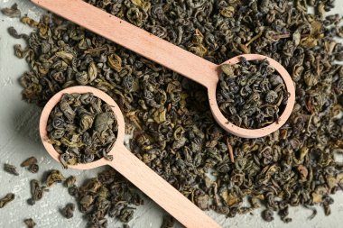 Ahşap kaşıklar, kuru yeşil çay yaprakları ve grunge yeşil arka plan.