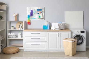 Çamaşır odasının içinde tahta, temizlik malzemeleri ve çamaşır makinesi var.