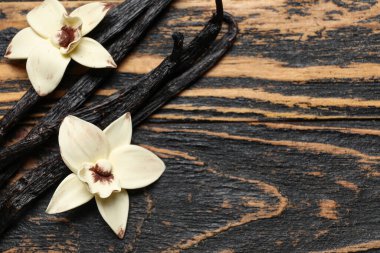 Siyah ahşap arka planda Aromatik vanilya çubukları ve çiçekler