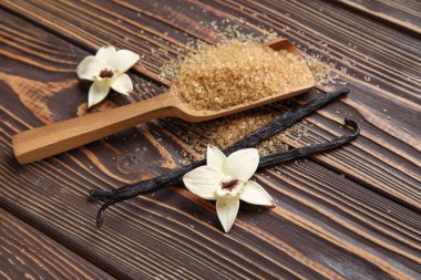 Spoon with aromatic vanilla sugar, flowers and sticks on wooden background clipart