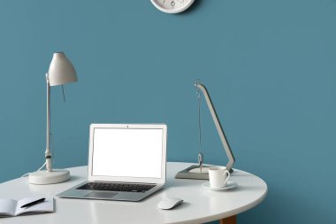 Modern dizüstü bilgisayarı, not defteri ve renkli duvarın yanında bir fincan kahvesi olan şık bir iş yeri.