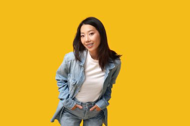 Sarı arka planda şık kot elbiseli güzel, mutlu Asyalı kadın.