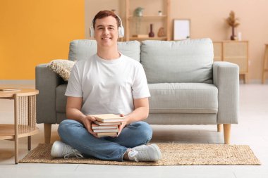 Genç adam sesli kitap dinliyor ve oturma odasında kitap tutuyor.