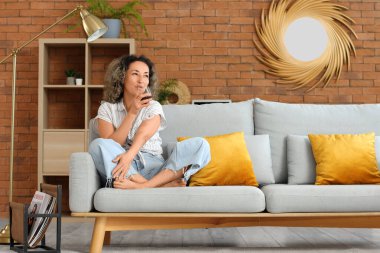 Evdeki kanepede oturan orta yaşlı, güzel bir kadın.