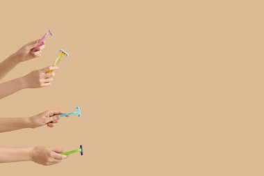 Bej arka planda farklı jiletler tutan kadın eller.