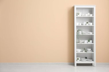 Bej duvarın yanında tabakları olan modern raf ünitesi.