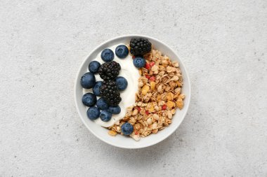 Bir kase lezzetli granola yoğurt ve arkaplanda böğürtlen.