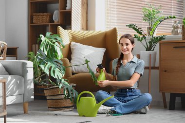 Evdeki Monstera bitkisine su püskürten güzel genç bir kadın.