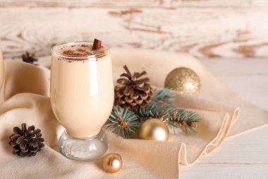 Tarçın, kozalak, köknar dalı ve beyaz ahşap arka planda noel toplarıyla bir bardak nefis eggnog kokteyli.