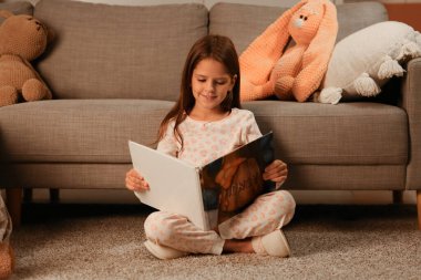 Oturma odasında yerde oturmuş peri masalı okuyan tatlı küçük kız.