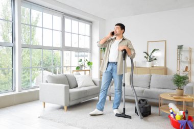 Evde elektrikli süpürgeyle konuşan genç bir adam.