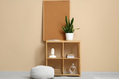 Bej duvarın yanındaki raflarda eski kitaplar ve heykelcikler var.