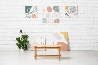 Sanat galerisinin içinde resimler, bitki ve bank var.