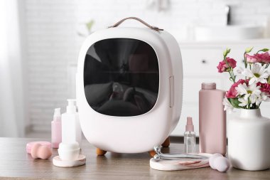 Cilt ürünleriyle kaplı kapalı kozmetik buzdolabı ve beyaz duvarın yanındaki masada vazoda çiçekler. Yakın çekim.