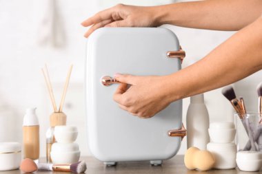 Beyaz arka planda, küçük kozmetik buzdolabı olan bir kadın eli. Yakın çekim.