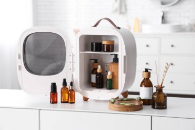 Küçük kozmetik buzdolabı, yüz gerdirme silindiri ve masa üzerinde beyaz arka planda gerekli yağ. Yakın çekim.