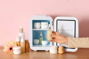 Kadın eller pembe arka planda küçük kozmetik buzdolabından serum alıyor. Yakın çekim.