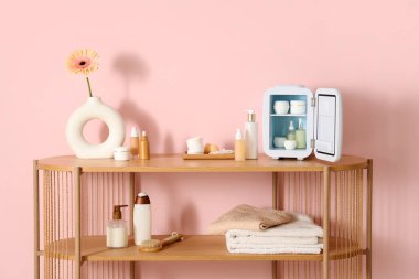 Cilt ürünleri ve vazodaki çiçekli açık kozmetik buzdolabı. Odadaki pembe duvarın yanındaki masada. Yakın çekim.