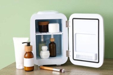 Masada yeşil arka planda kozmetik ürünleri olan küçük bir buzdolabı aç. Yakın çekim.