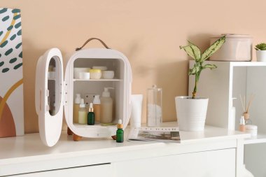 Bej duvarın yanındaki çekmecelerde kozmetik ürünleri olan küçük bir buzdolabı aç. Yakın çekim.