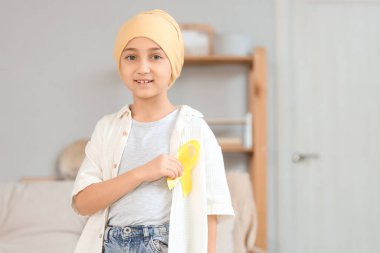 Evde sarı kurdeleli kemoterapiden sonra küçük bir kız. Çocukluk kanseri farkındalığı