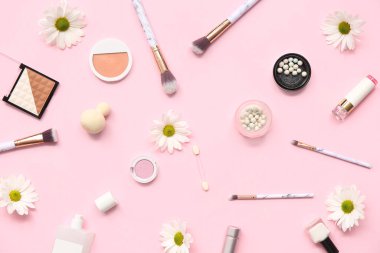Pembe arka planda makyaj ürünleri, fırçalar ve çiçeklerle kompozisyon