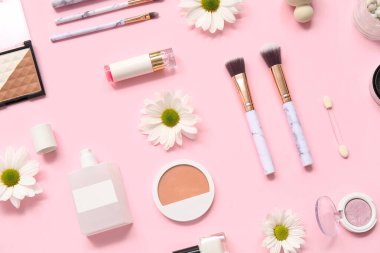 Makyaj ürünleri, parfüm şişeleri ve pembe arka planda çiçekler.