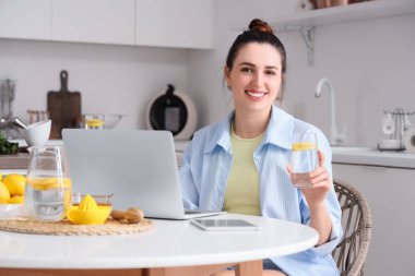 Mutfakta limonlu su ve dizüstü bilgisayarı olan güzel bir kadın.