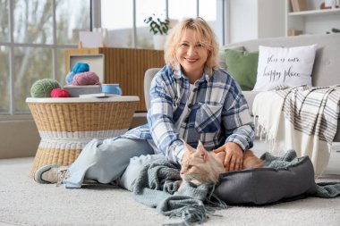 Evcil hayvan yatağında sevimli bir kedinin yanında oturan orta yaşlı güzel bir kadın.