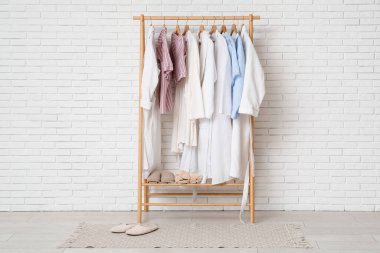 Beyaz tuğla duvarın yanında pijama, bornoz ve terliklerle dizilin.