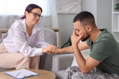 Travma sonrası stres bozukluğu olan erkek asker ve ofiste el ele tutuşan psikolog.