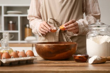 Kadın mutfak tezgahında hamur hazırlamak için yumurtayı kaseye kırıyor.