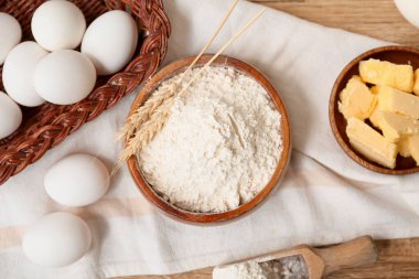 Tahta arka planda hamur hazırlamak için bir kase un, yumurta ve tereyağı.