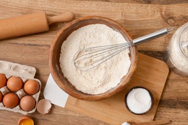 Tahta zemin üzerinde hamur hazırlamak için çırpılmış un, yumurta, tuz ve merdane.