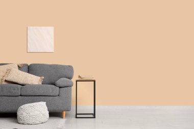 Bej duvarın yanında rahat kanepe, puf ve kahve masası olan şık bir oturma odası.