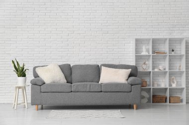 Rahat kanepesi, raf ünitesi ve beyaz tuğla duvarın yanındaki ev bitkisi olan şık bir oturma odası.