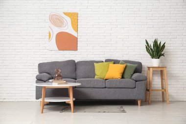 Rahat kanepesi, sehpası ve beyaz tuğla duvarın yanında bitkisi olan şık bir oturma odası.