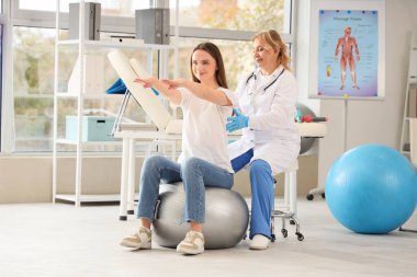 Olgun kadın osteopat klinikte topa uygun genç bir kadınla egzersiz yapıyor.