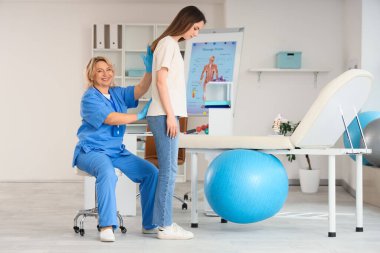 Klinikte genç bir kadınla çalışan olgun, mutlu bir kadın osteopat.