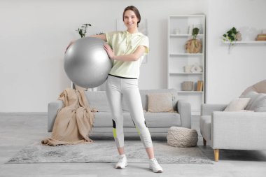Sportif genç bir kadın evde spor topu tutuyor.