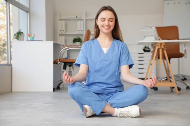 Genç bayan doktor klinikte yerde meditasyon yapıyor.
