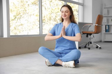 Genç bayan doktor klinikte yerde meditasyon yapıyor.