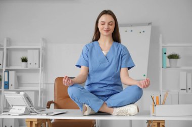 Genç bayan doktor klinikteki masada meditasyon yapıyor.
