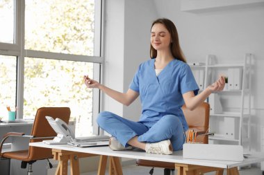 Genç bayan doktor klinikteki masada meditasyon yapıyor.