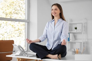 Genç iş kadını ofiste masa başında meditasyon yapıyor.