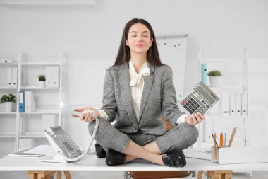 Hesap makinesi ve telefon ile genç iş kadını modern ofisteki masada meditasyon yapıyor.