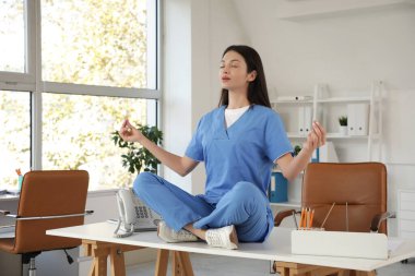 Genç bayan doktor klinikteki masada meditasyon yapıyor.